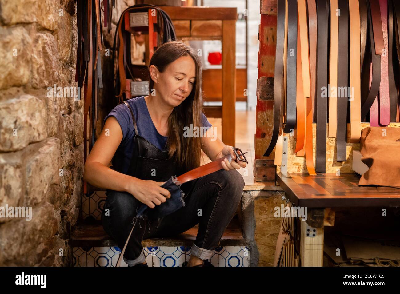 Young leather craftswoman in her traditional workshop holding a handmade belt Stock Photo