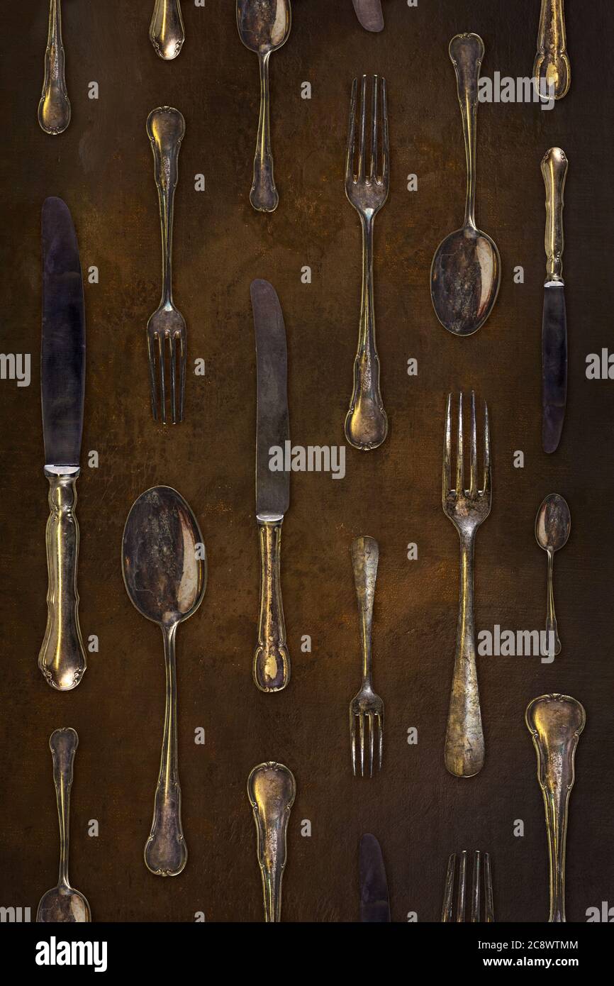 Vintage styled image of old forks, knives and spoons in a repetitive pattern on a dark brown background Stock Photo