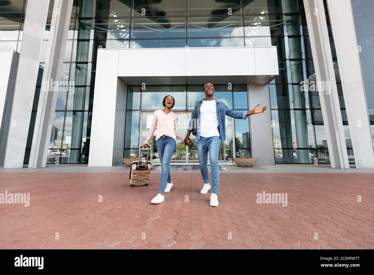 After Arrival. Joyful black couple leaving airport terminal with ...