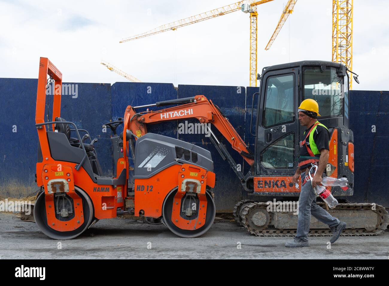 Construction worker walking through a red colored excavator and roller