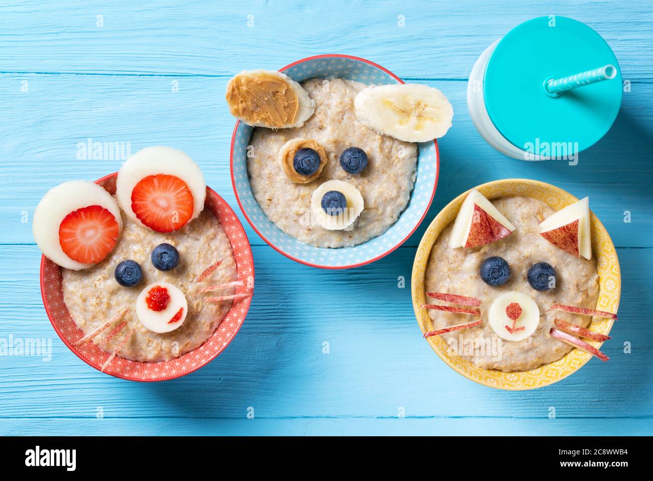 Funny bowls with oat porridge with cat, dog and mouse faces made of fruits and berries, food for kids idea, top view Stock Photo