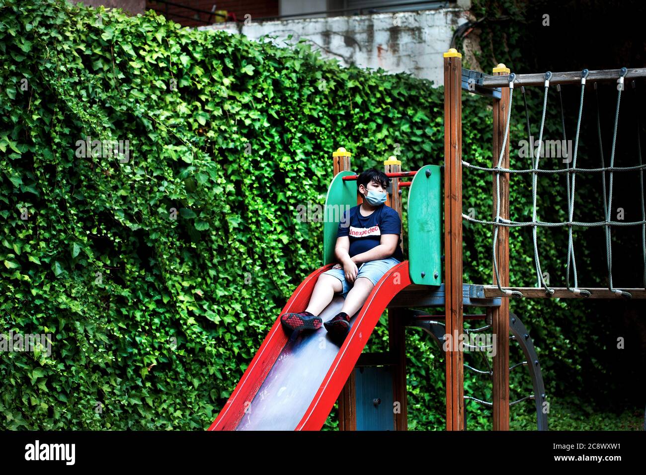 Boy sat alone on slide wearing face mask, Barcelona Stock Photo Alamy