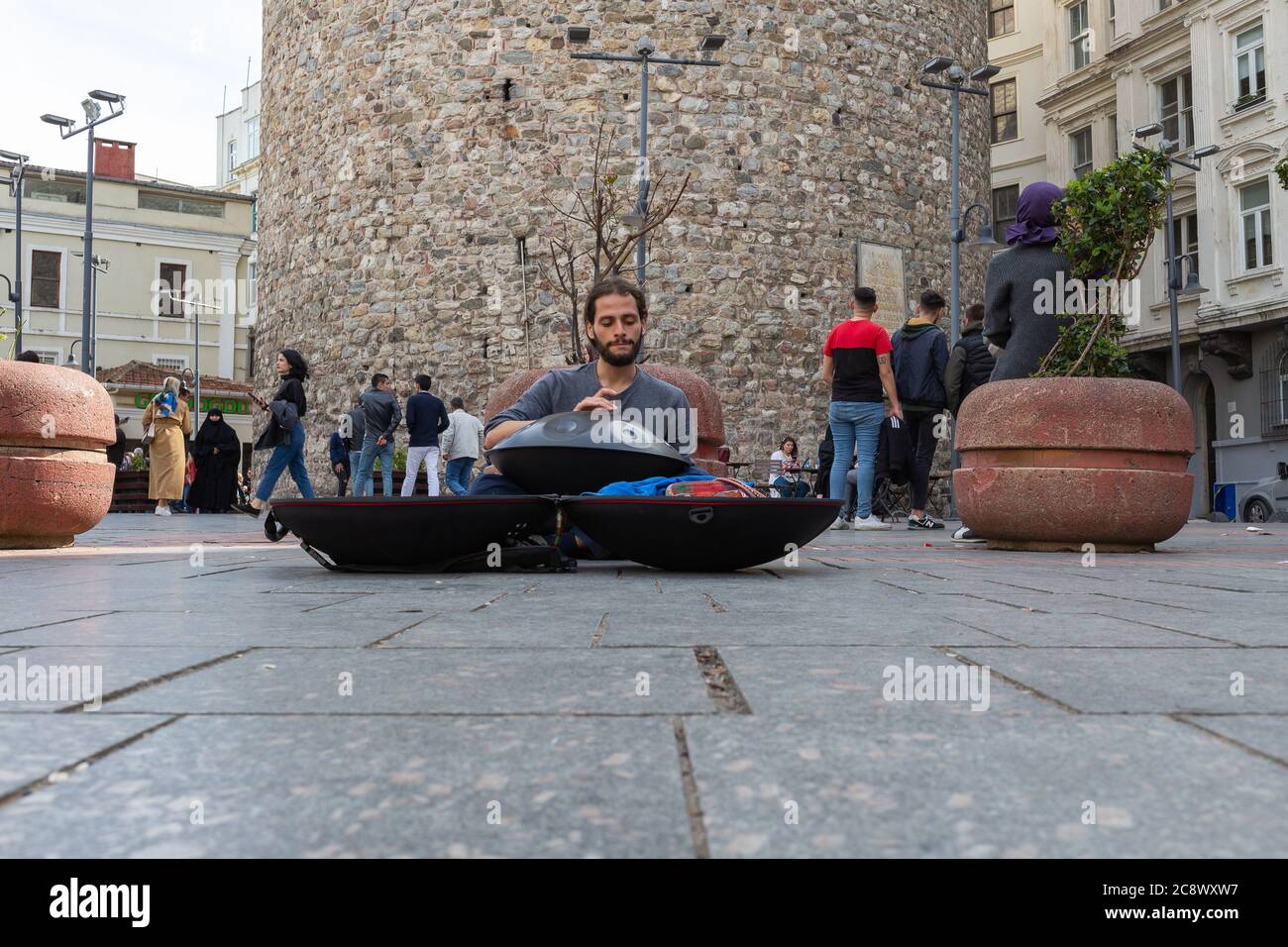 Young street musician playing hang drum under Galata Tower while