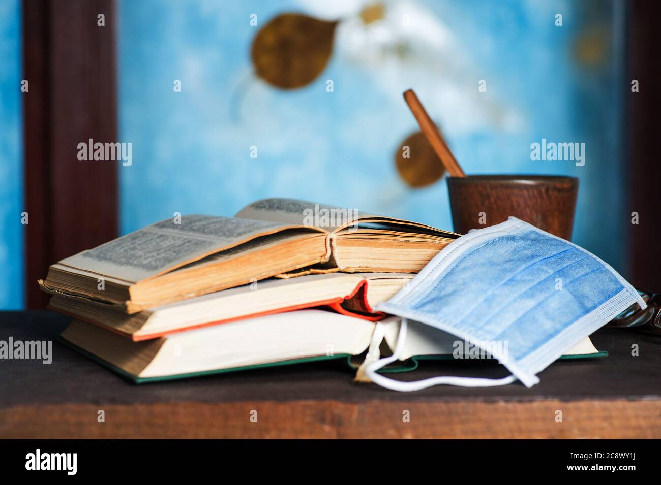 Open book and a warm drink with a face mask on a table with autumn background Stock Photo