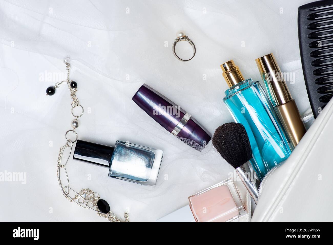 Various makeup and cosmetic fall out of an female bag tabletop flat lay. Perfume lipsticks nail polishes with brushes an other accessories Stock Photo
