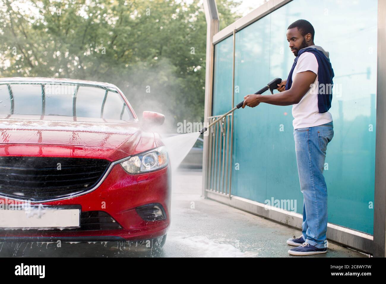Handsome African guy in t-shirt and jeans washing his red luxury car,  rinsing the soap with high pressure water jet. Manual car wash with  pressurized Stock Photo - Alamy