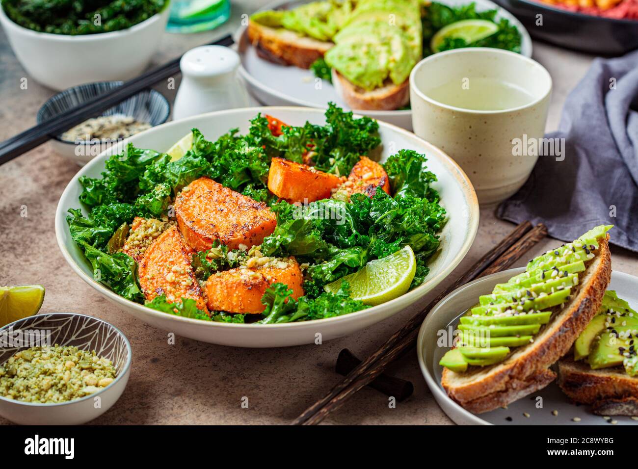 Vegan lunch table. Baked sweet potato salad with kale, avocado toast and hummus on a dark background. Stock Photo
