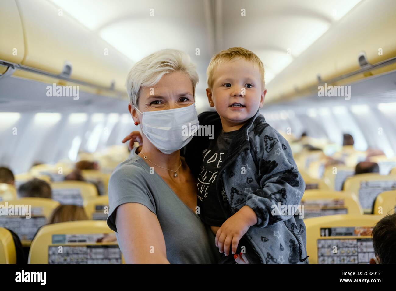 Mother wearing mask holding years old son in the airplane hires stock