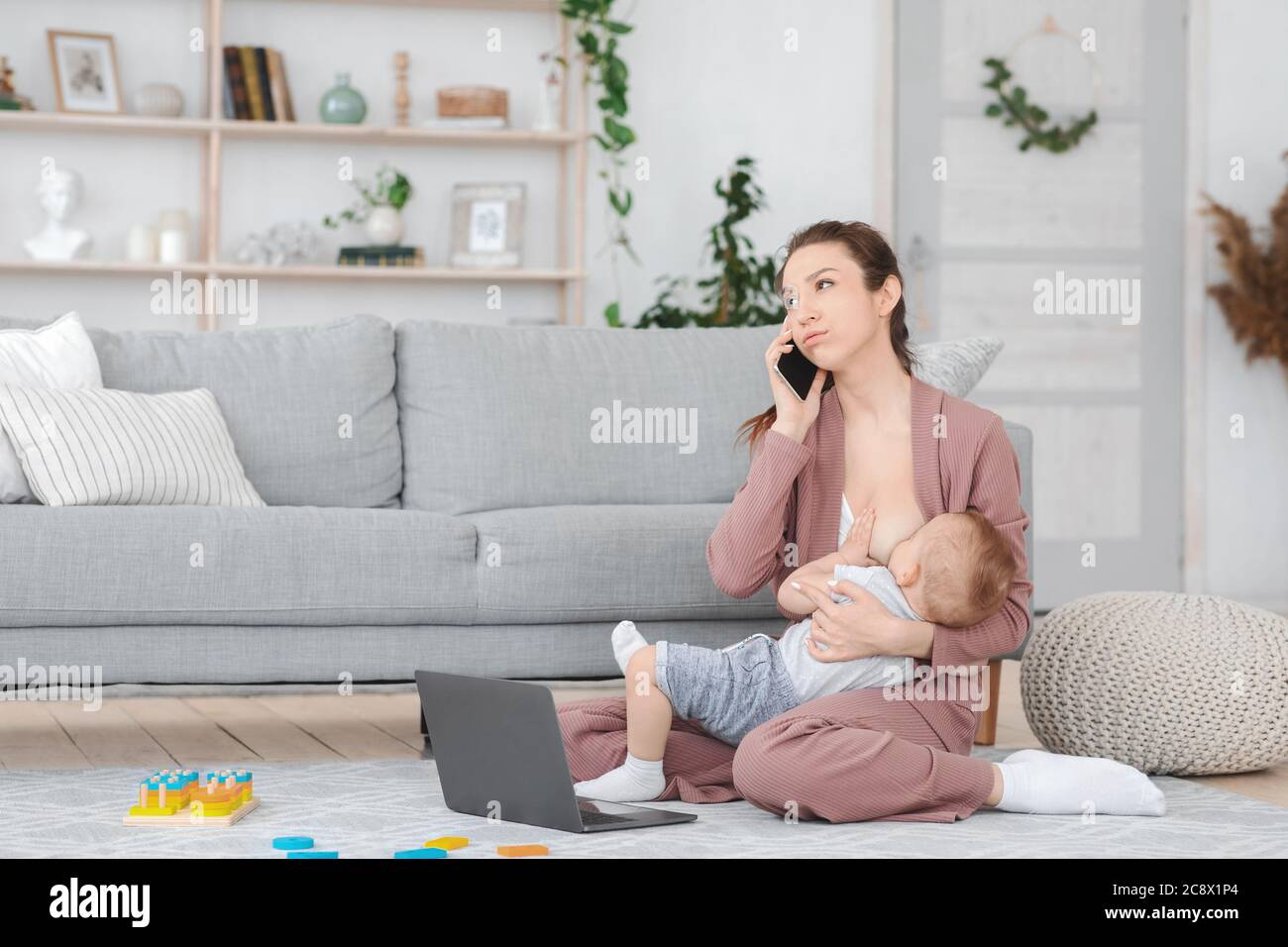 Motherhood Frustration. Bored Woman Breastfeeding Baby And Talking On Cellphone At Home Stock Photo