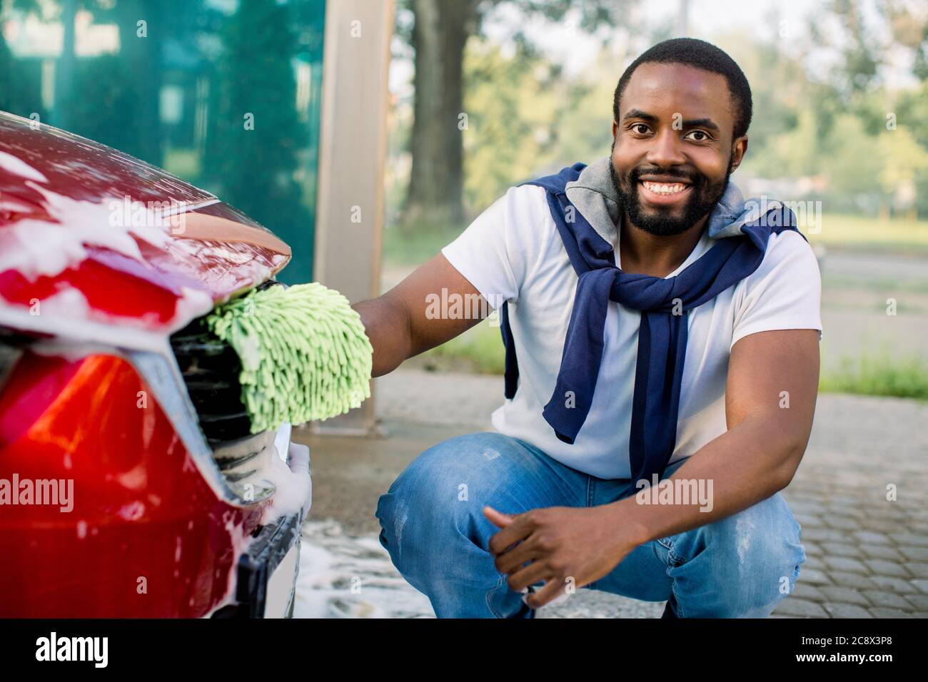 Car detailing wash at outdoors car wash service. Smiling handsome African American black man in