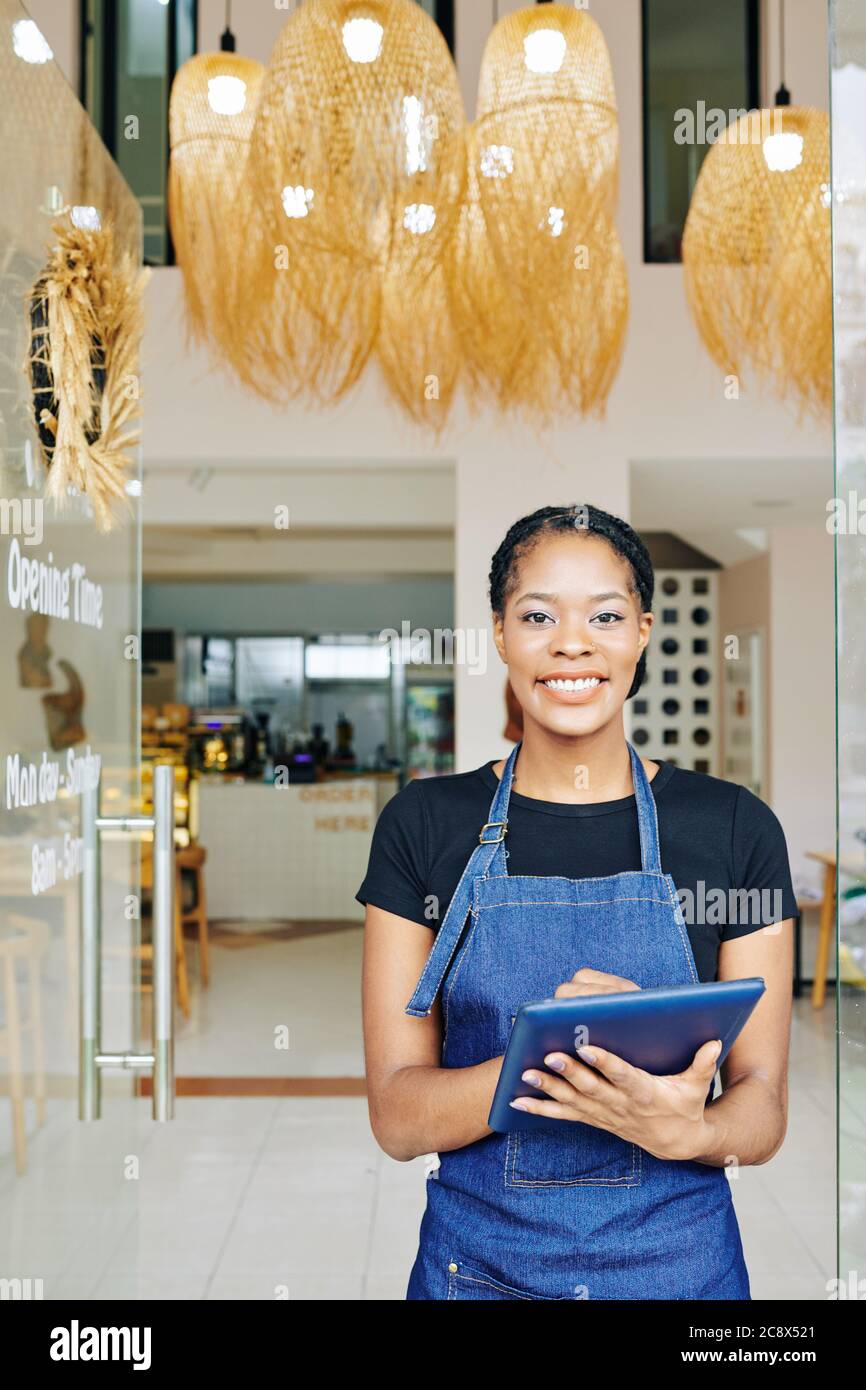 Happy smiling pretty waitress using application on tablet computer when working in cafe Stock Photo