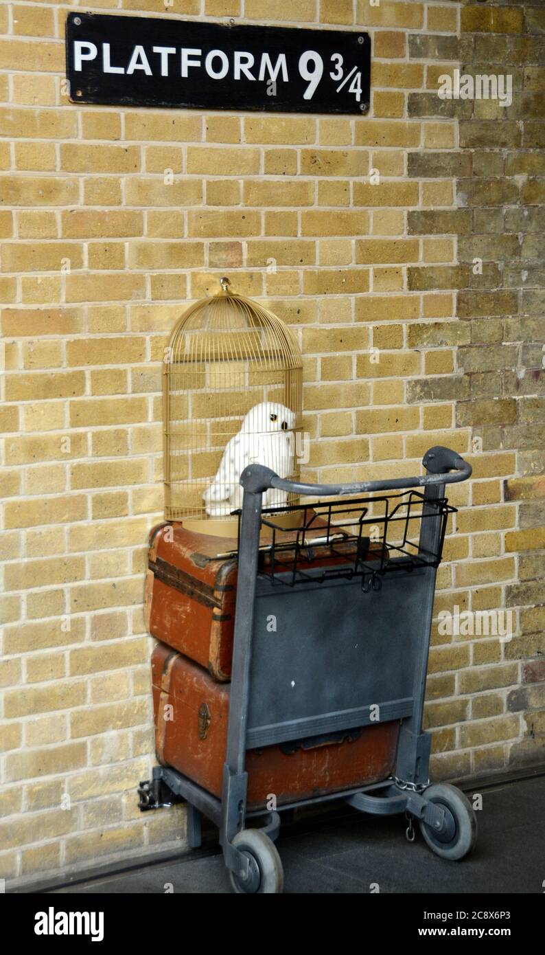 Platform 9 and 3/4 is located at King's Cross St. Pancras station. The baggage cart is halfway stuck in the wall and Edwige's cage in plain sight. Stock Photo