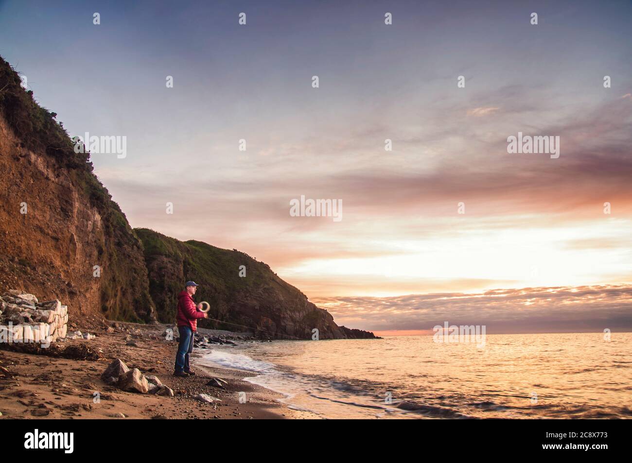 Morning fishing. Man with hand reel fishing at sunrise on a sea beach. Stock Photo