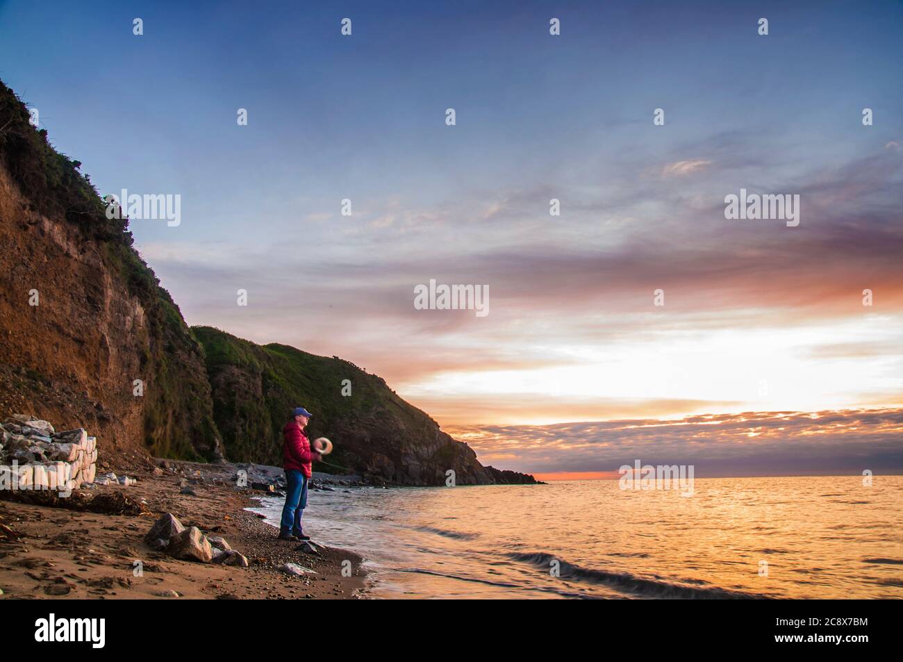 Morning fishing. Man with hand reel fishing at sunrise on a sea beach. Stock Photo