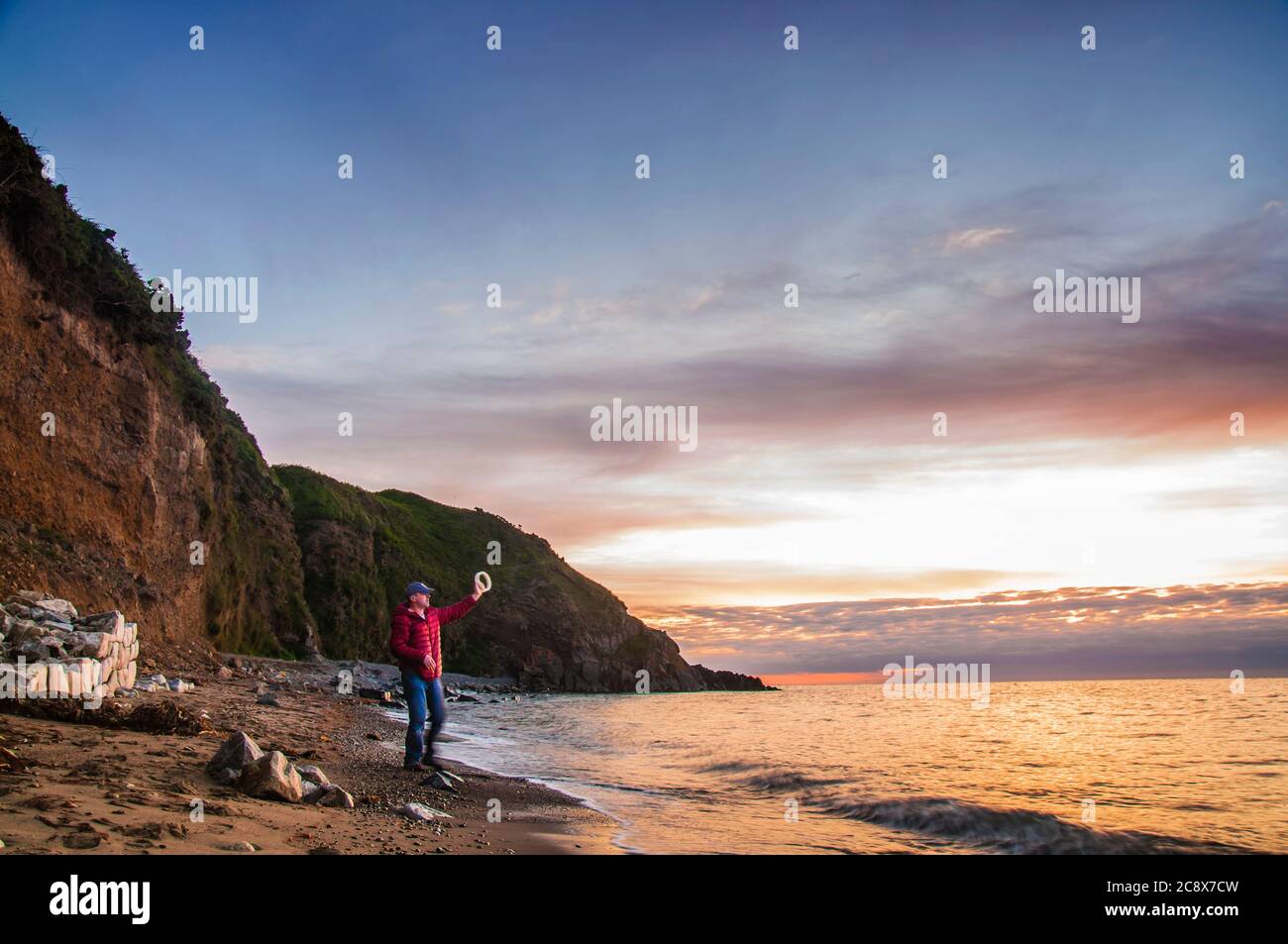 Morning fishing. Man with hand reel fishing at sunrise on a sea beach. Stock Photo