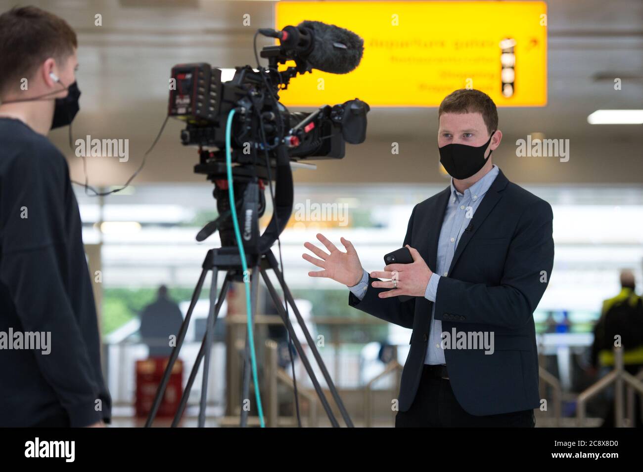 Glasgow, Scotland, UK. 27th July, 2020. Pictured: BBC News Reporter, Connor Gillies, seen delivering a live news report on camera in the terminals departures area. Inside Glasgow Airport's terminal 1. The Scottish Government announced as from 00:01 this morning that all incoming flights from Spain into Scotland would need a period of 14 days quarantine. Jet2 Airlines have operated a number of flights this morning and a further afternoon service to Tenerife despite the new travel restrictions. Credit: Colin Fisher/Alamy Live News Stock Photo