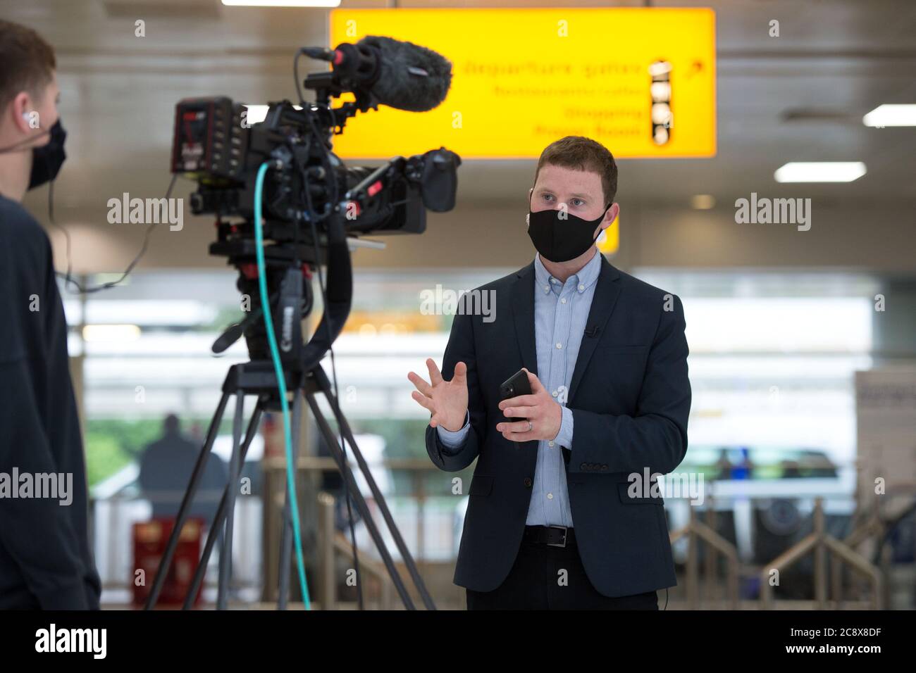 Glasgow, Scotland, UK. 27th July, 2020. Pictured: BBC News Reporter, Connor Gillies, seen delivering a live news report on camera in the terminals departures area. Inside Glasgow Airport's terminal 1. The Scottish Government announced as from 00:01 this morning that all incoming flights from Spain into Scotland would need a period of 14 days quarantine. Jet2 Airlines have operated a number of flights this morning and a further afternoon service to Tenerife despite the new travel restrictions. Credit: Colin Fisher/Alamy Live News Stock Photo