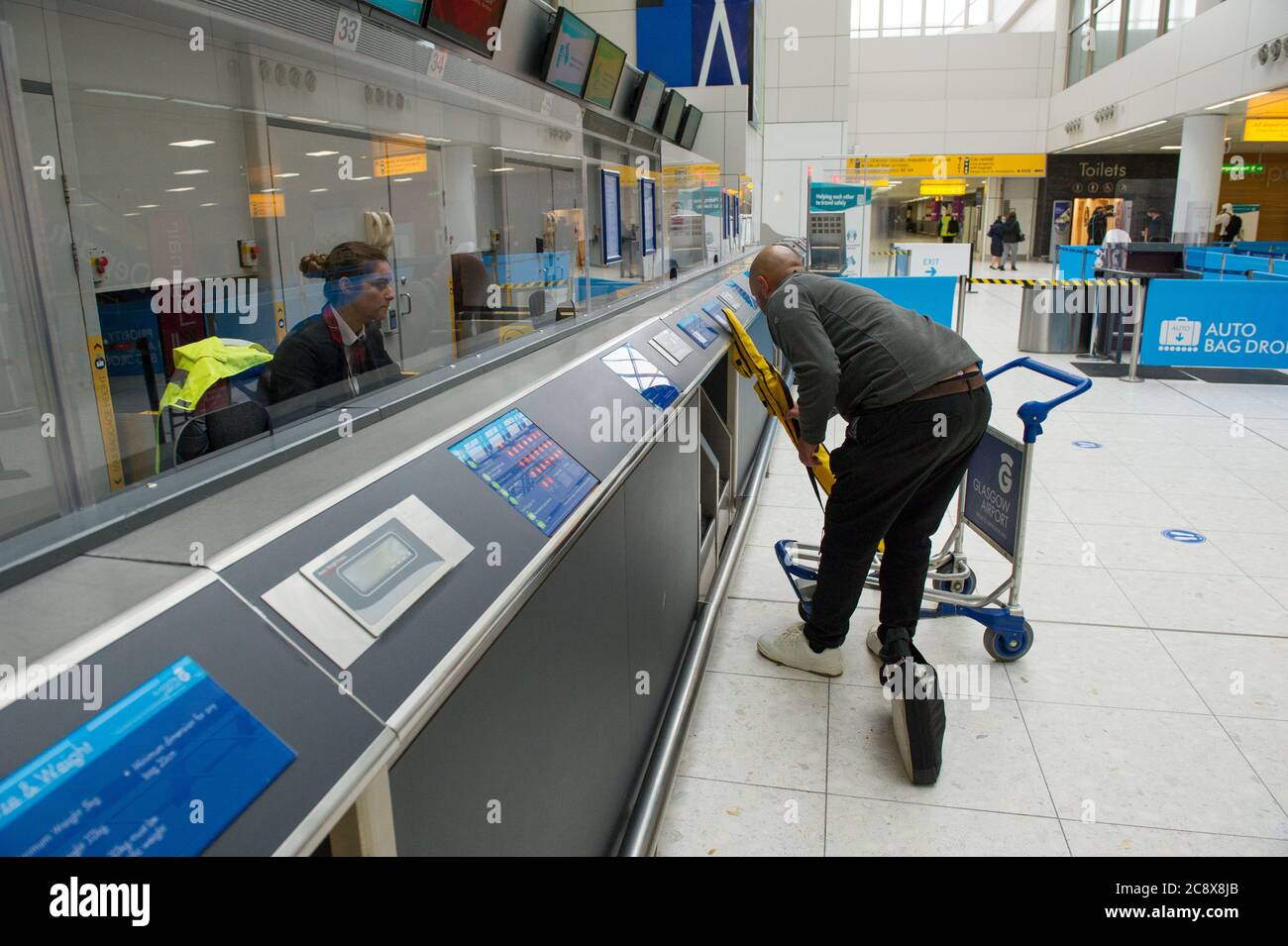 Glasgow, Scotland, UK. 27th July, 2020. Pictured: A passenger checks in for his flight at the newly adapted desks which have clear perspex screens to protect airport workers and maintain social distancing. Inside Glasgow Airport's terminal 1. The Scottish Government announced as from 00:01 this morning that all incoming flights from Spain into Scotland would need a period of 14 days quarantine. Jet2 Airlines have operated a number of flights this morning and a further afternoon service to Tenerife despite the new travel restrictions. Credit: Colin Fisher/Alamy Live News Stock Photo