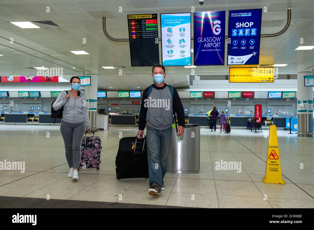 Glasgow, Scotland, UK. 27th July, 2020. Pictured: Passengers wearing blue surgical face masks seen wheeling their luggage in the airport terminal. Inside Glasgow Airport's terminal 1. The Scottish Government announced as from 00:01 this morning that all incoming flights from Spain into Scotland would need a period of 14 days quarantine. Jet2 Airlines have operated a number of flights this morning and a further afternoon service to Tenerife despite the new travel restrictions. Credit: Colin Fisher/Alamy Live News Stock Photo