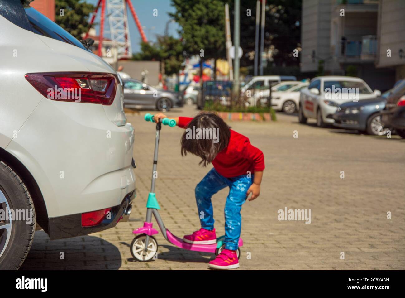 Little girl leaning under the car with scooter Stock Photo