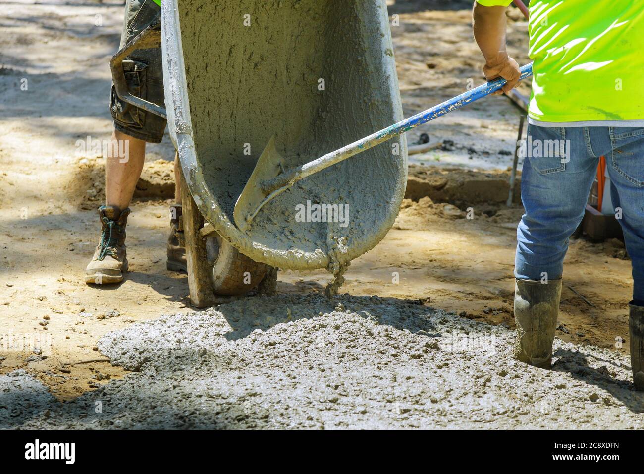 Process worker pour cement for sidewalk in concrete works with new pavement, wheelbarrow of mortar for pouring the foundation Stock Photo