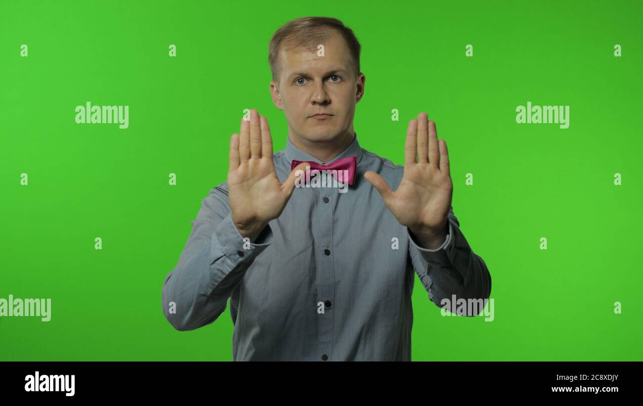 Guy showing stop gesture with hands. No, never, disliking and rejecting sign. Portrait of man 30s posing in shirt isolated on chroma key background in studio. People emotions Stock Photo