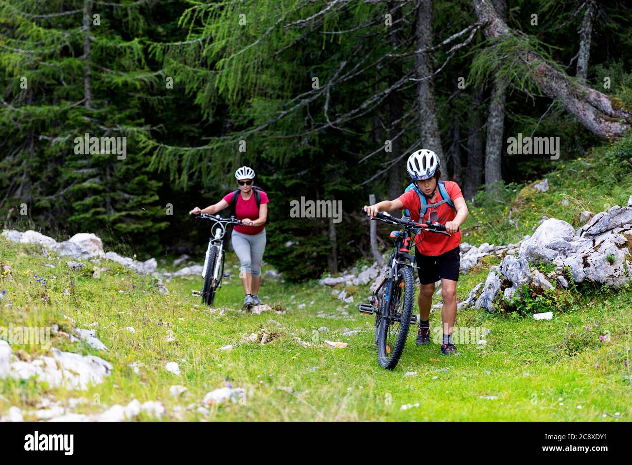 Mother and son pushing bikes on steep terraing trough the forest Stock Photo