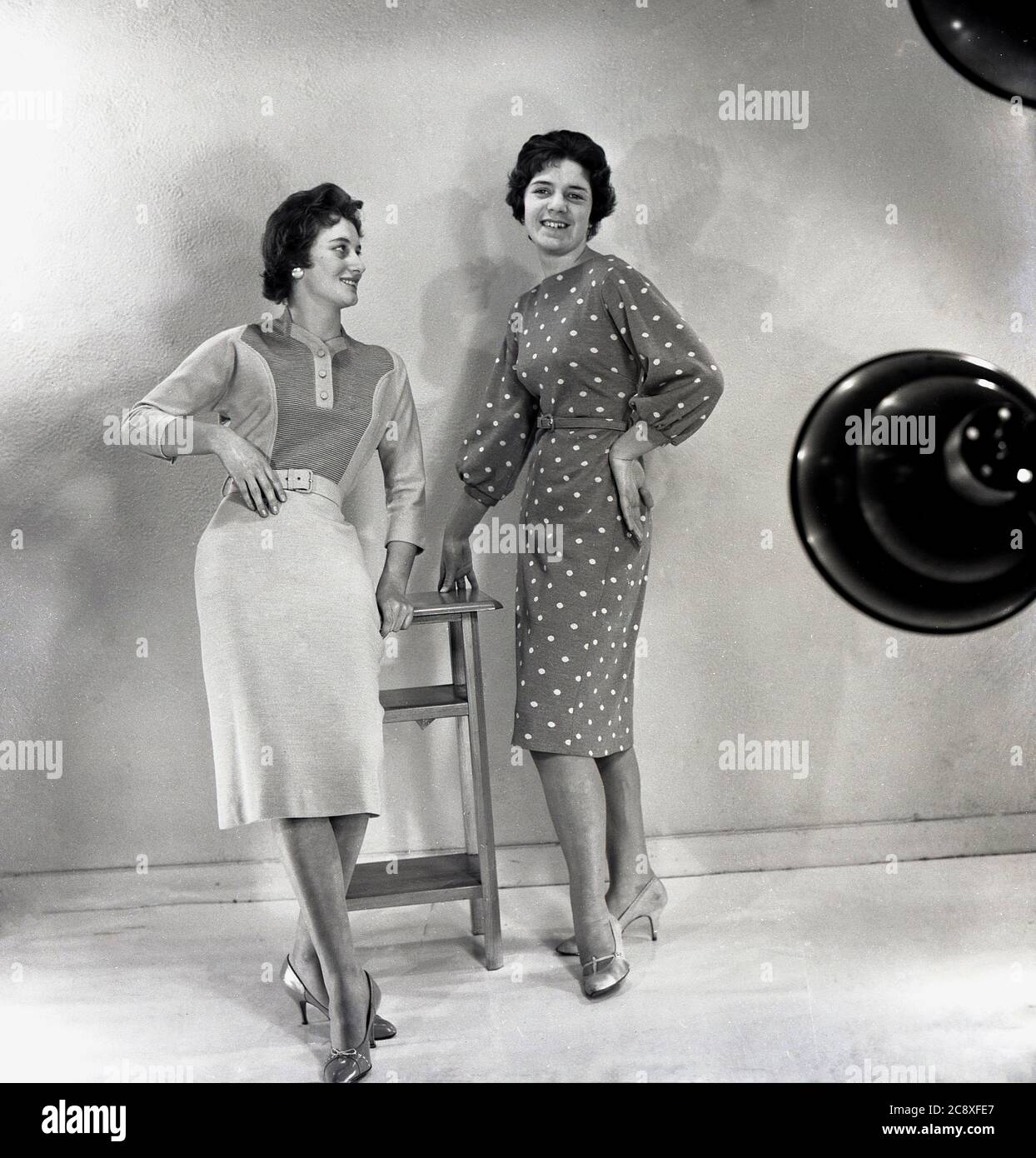 1950s, historical, two young ladies in a studio modelling the latest female fashions, including a woollen top and skirt and spotted or polka dot dress, England, UK. Stock Photo