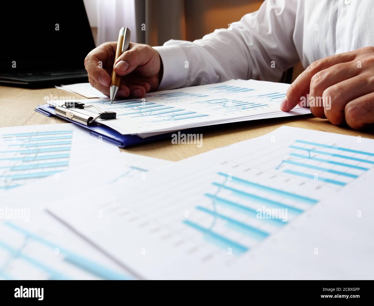 A man in a white shirt checks financial charts and tables at the table. Paperwork and reporting. Stock Photo