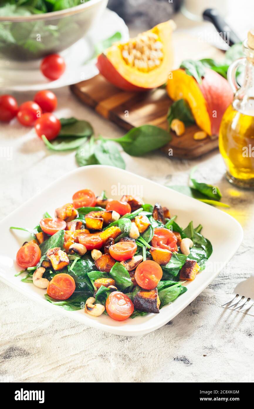 Roasted pumpkin salad with spinach, tomatoes and nuts. Autumn dish Stock Photo