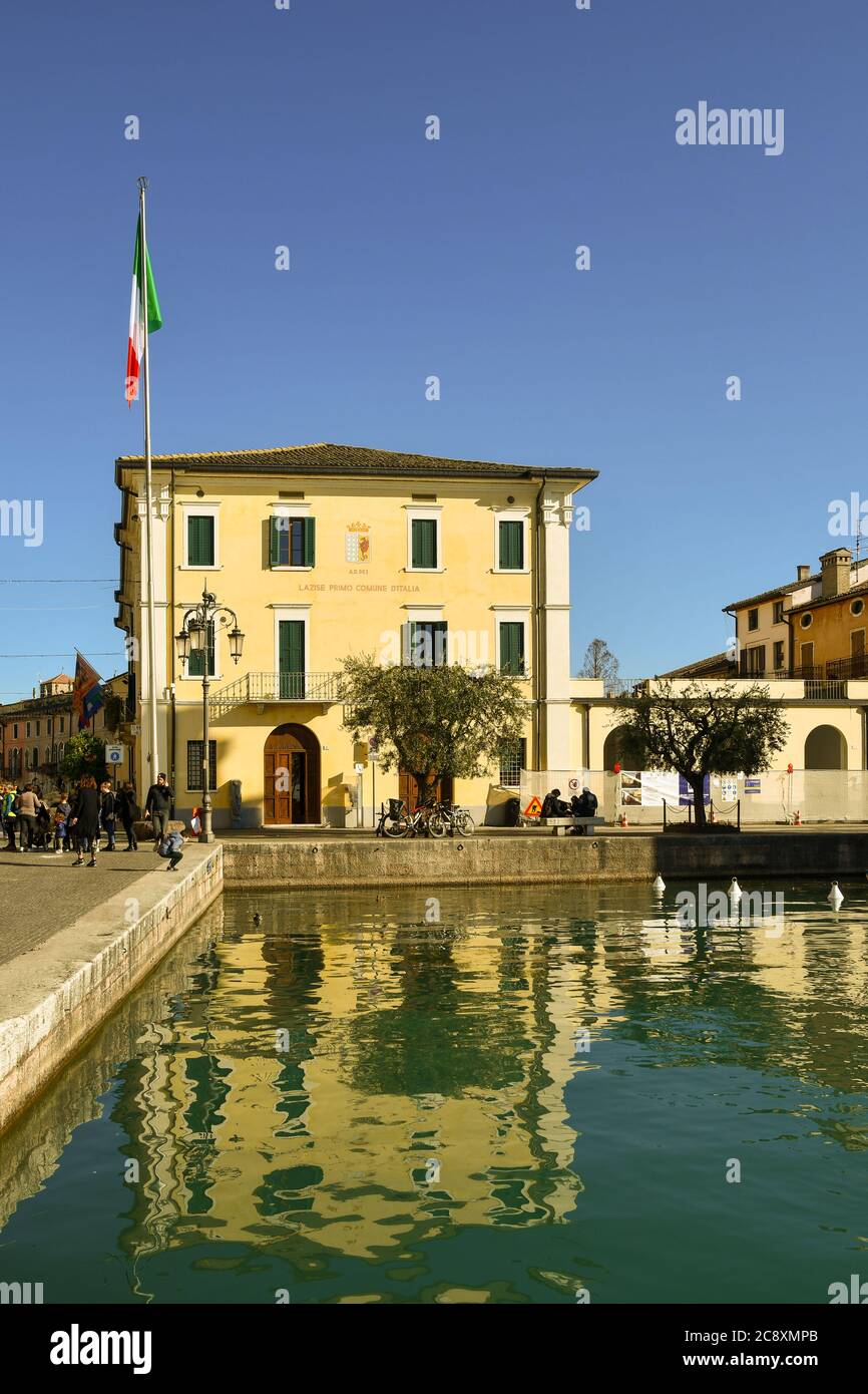 Facade of the city hall of the old town on the shore of Lake Garda with an Italian flag in a sunny day, Lazise, Verona, Veneto, Italy Stock Photo