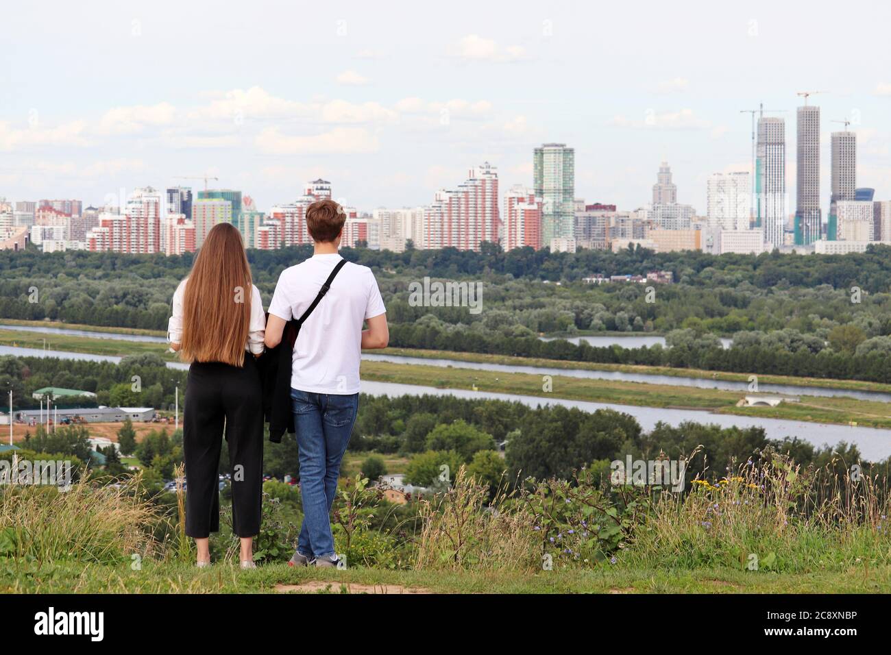 Young couple in love standing on top of a hill on a city background. Summer leisure and hiking, romantic date, future planning concept Stock Photo
