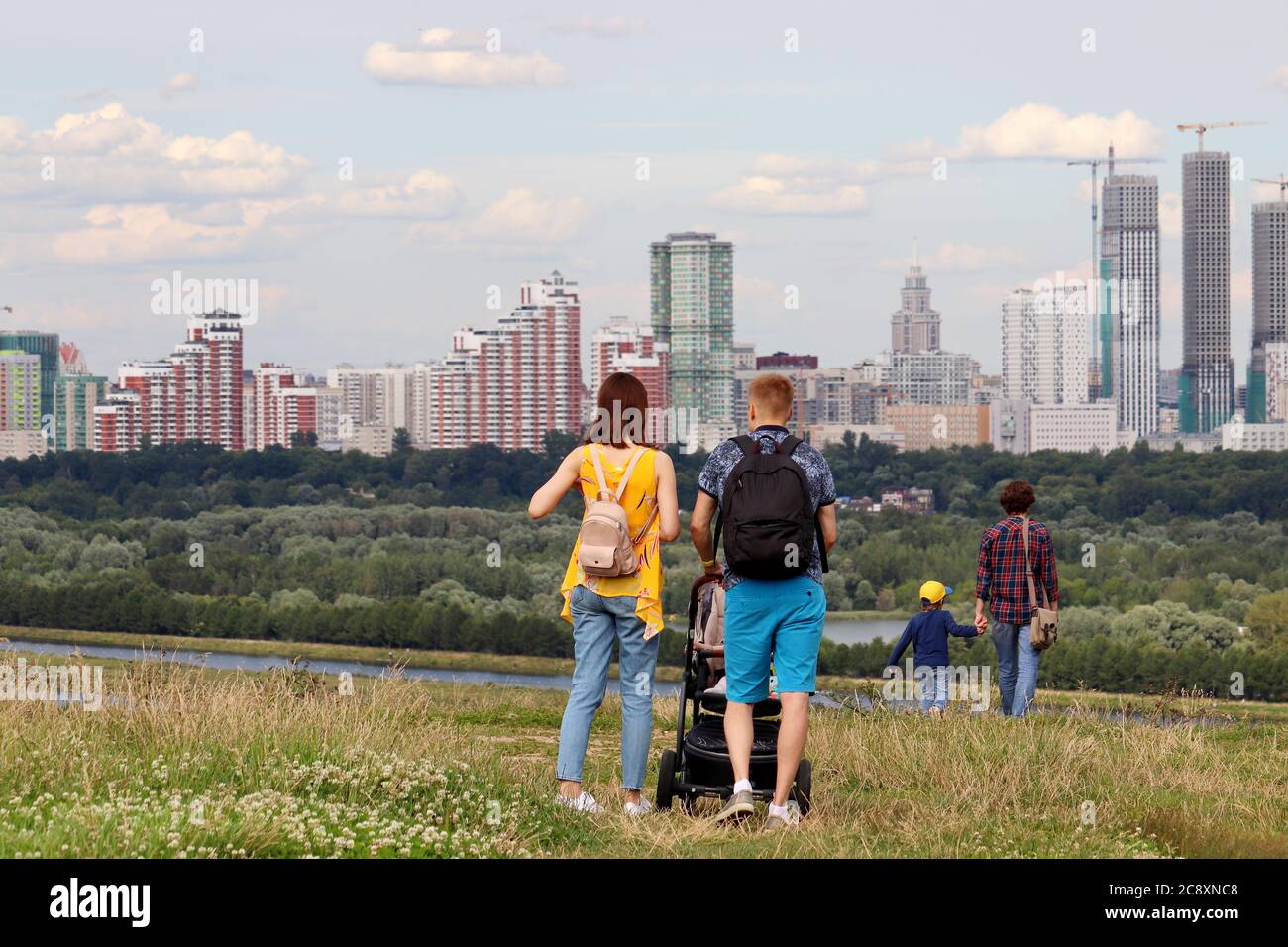 Couple in with baby pram walking on top of a hill on background of summer city and buildings under construction. Family leisure, real estate concept Stock Photo