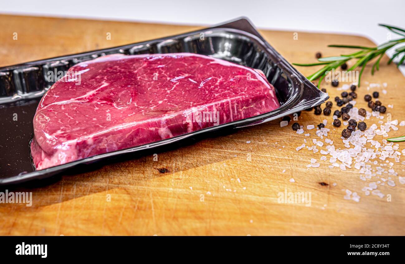 Beef steak in vacuum skin packaging and spices on wooden chopping board with copyspace Stock Photo