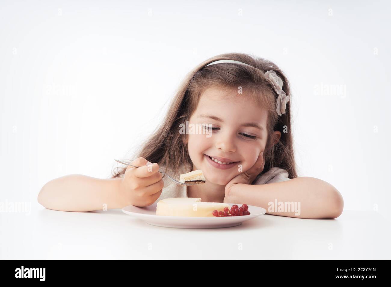 Beautiful little girl surprised from a tasty cheesecake. Kid ready to eat cake. Stock Photo