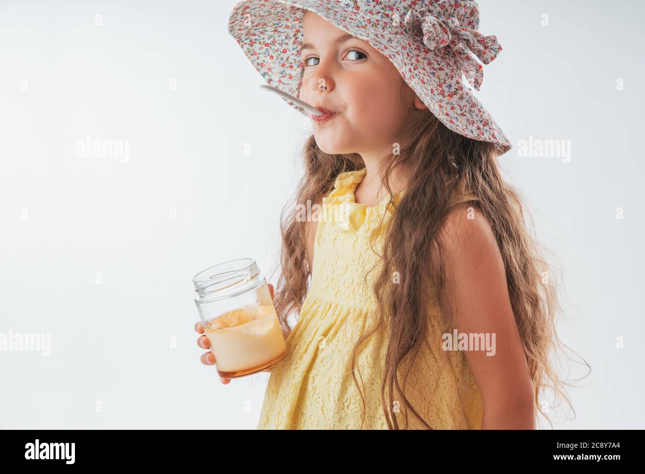 Beautiful little girl with spoon in mouth eating tasty cream. Eating yummy ice cream is fun Stock Photo