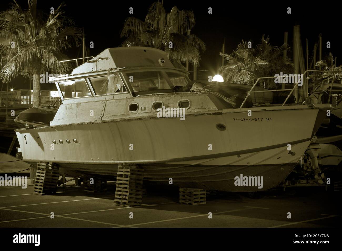 Boat in dry dock, inside the port surrounded by palm trees in monochrome and night shot. Stock Photo