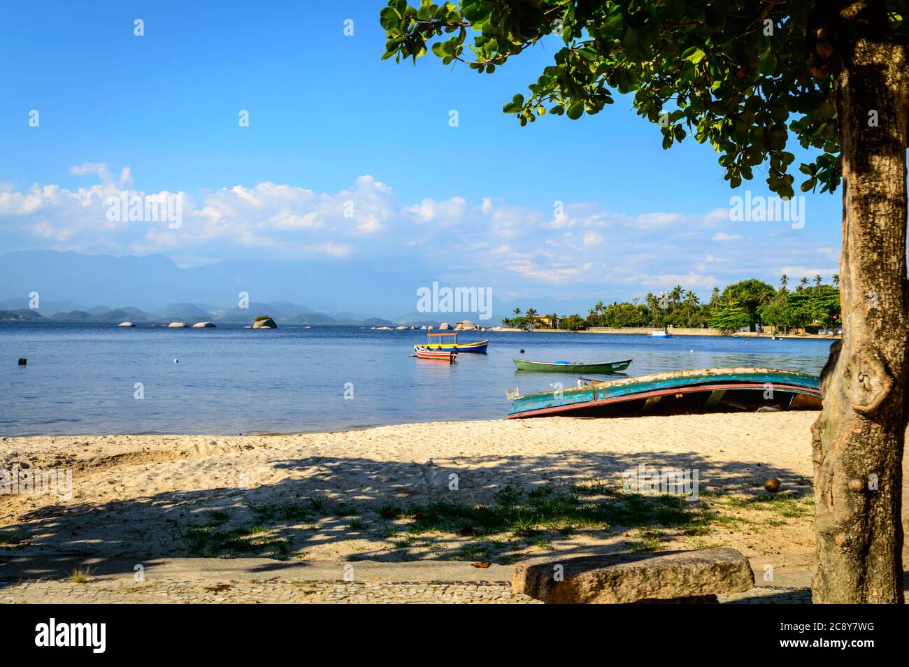 Tranquil beach sene with colorful wood boats, sand, shade, tree, calm water at Paquetá Island, Rio de Janeiro, Brazil. Stock Photo