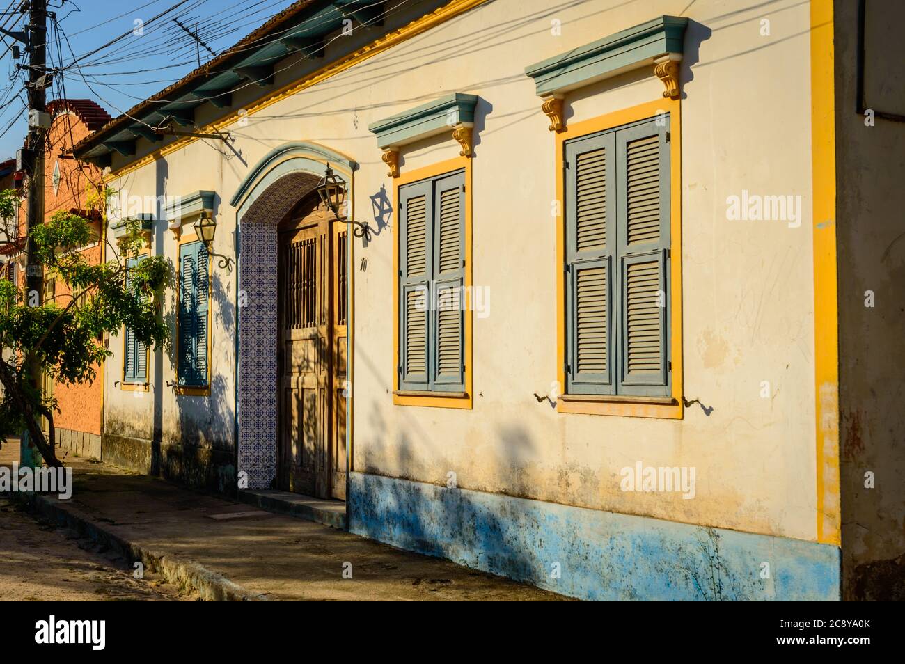 A Portuguese colonial home with blue window shutters and yellow trim and blue tile around the arch door. Stock Photo