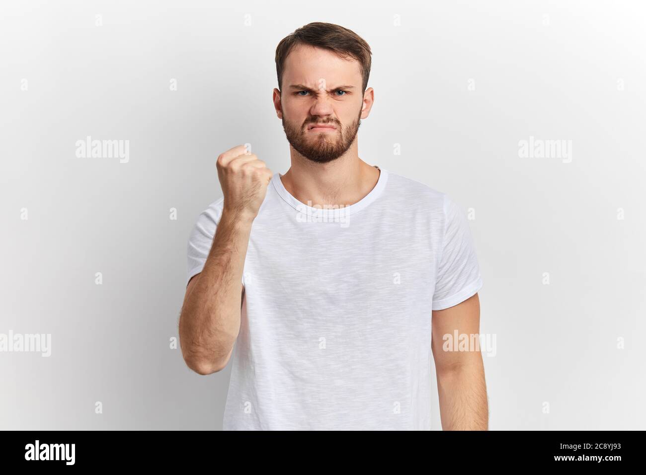 Angry nervous young man shows clenched fist, giving warning isolated on