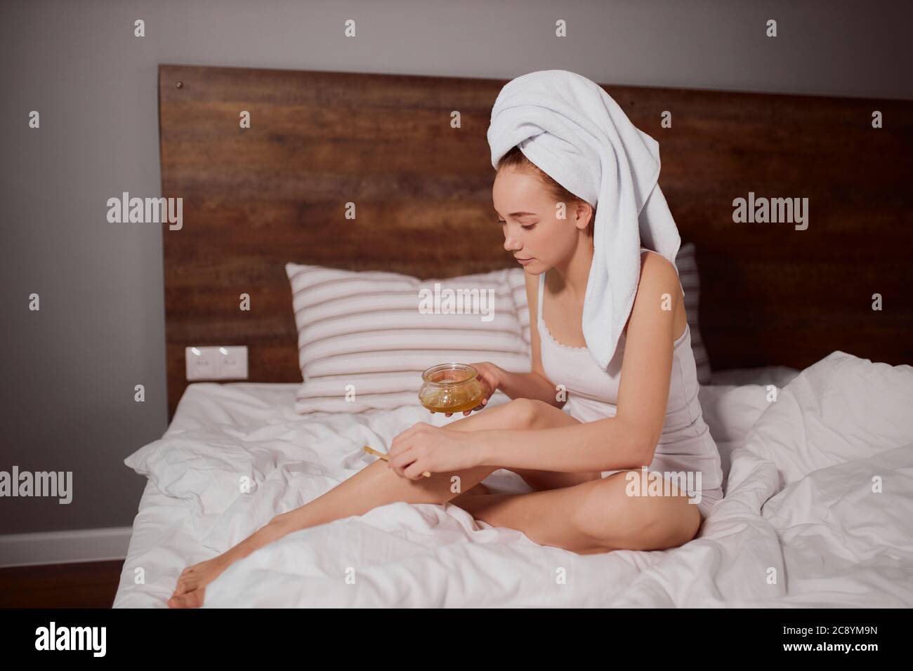 Attractive pleasant girl doing hairs removal procedure at home, sitting