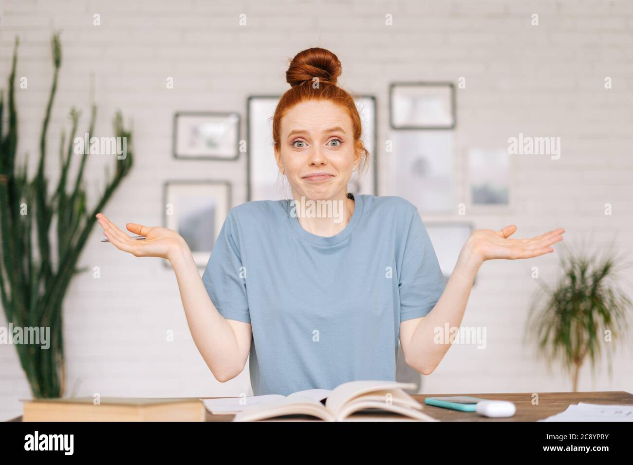 Happy surprised redhead young woman student sitting at a table with textbooks and a workbook Stock Photo