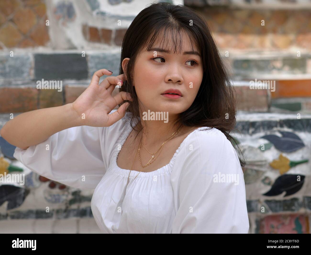 Pretty Southeast Asian girl looks over her shoulder at Bangkok’s Wat Arun Temple. Stock Photo