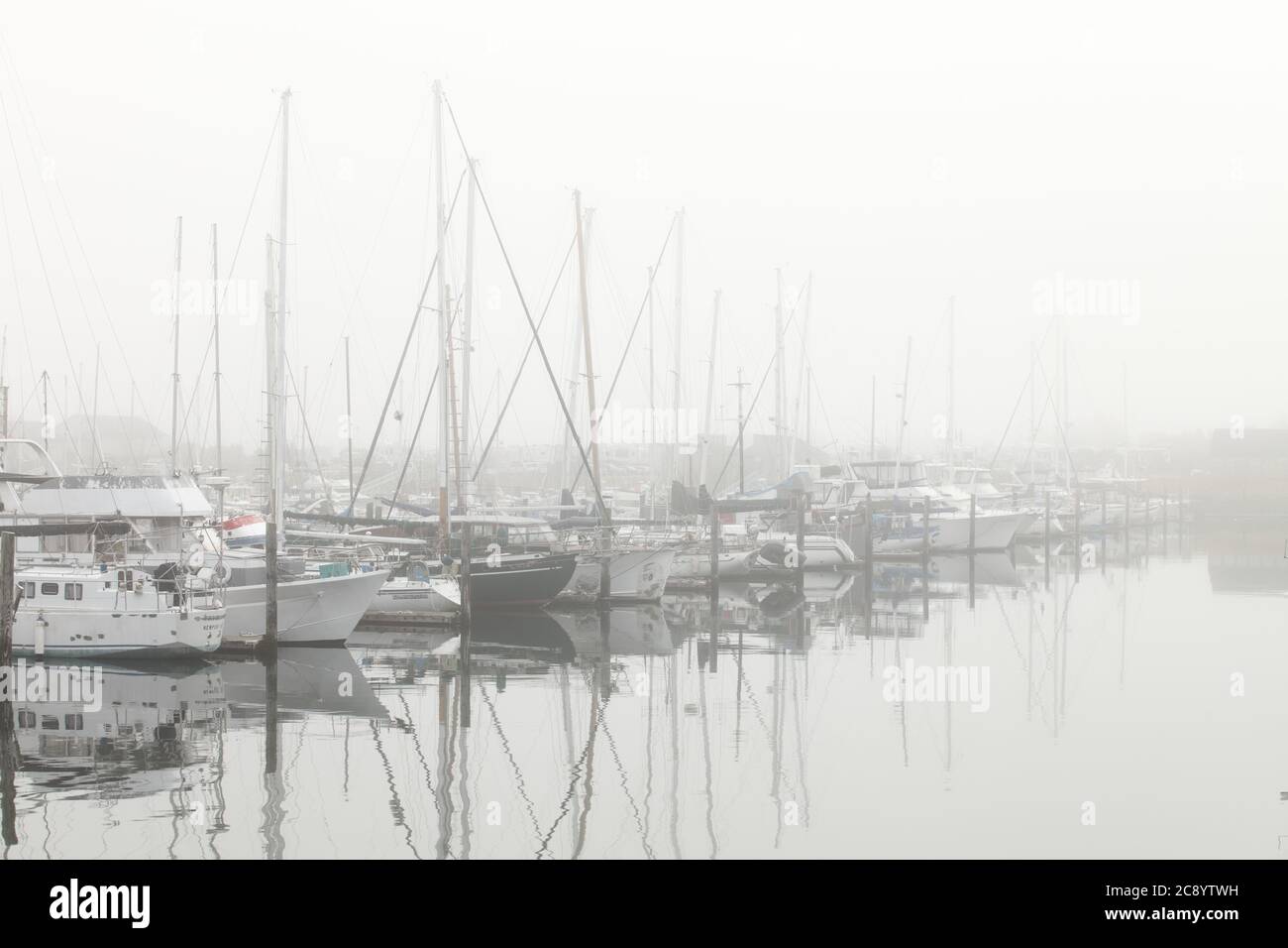 A foggy morning view of the Newport marina on the Yaquina river in Oregon.  There are many commercial and private fishing boats morred in the backgrou Stock Photo