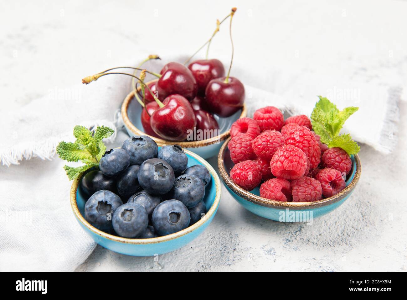 Assorted fresh juicy summer berries. Cherry, blueberry and raspberry in ceramic bowls, healthy snack concept. Stock Photo