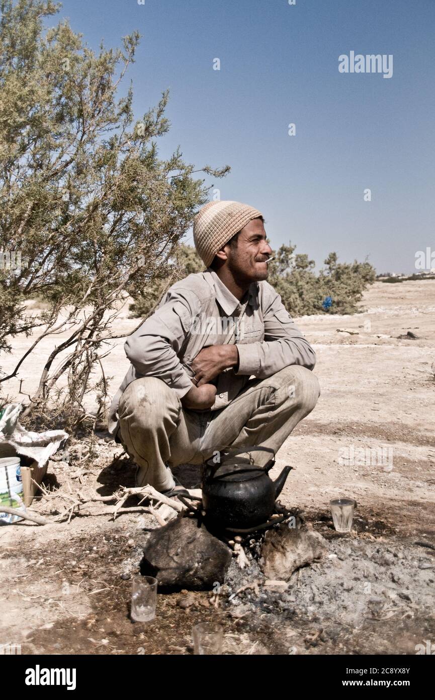 A young Bedouin man brewing tea and smoking a cigarette near the town of Azraq, in the Badia region of the Eastern Desert of Jordan. Stock Photo