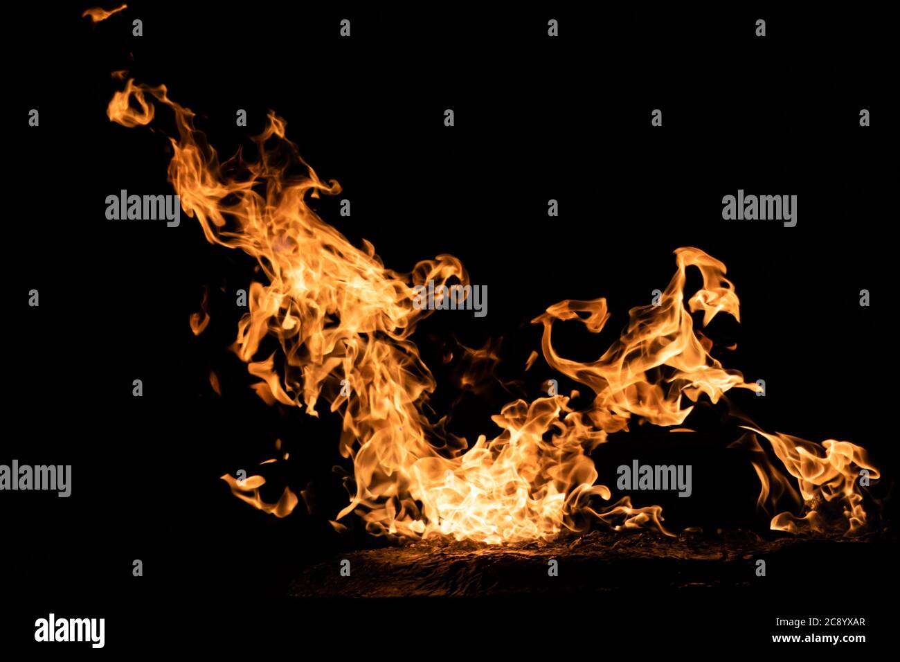 A bright, vibrant orange flame burns, the fire dancing on a black background. Stock Photo