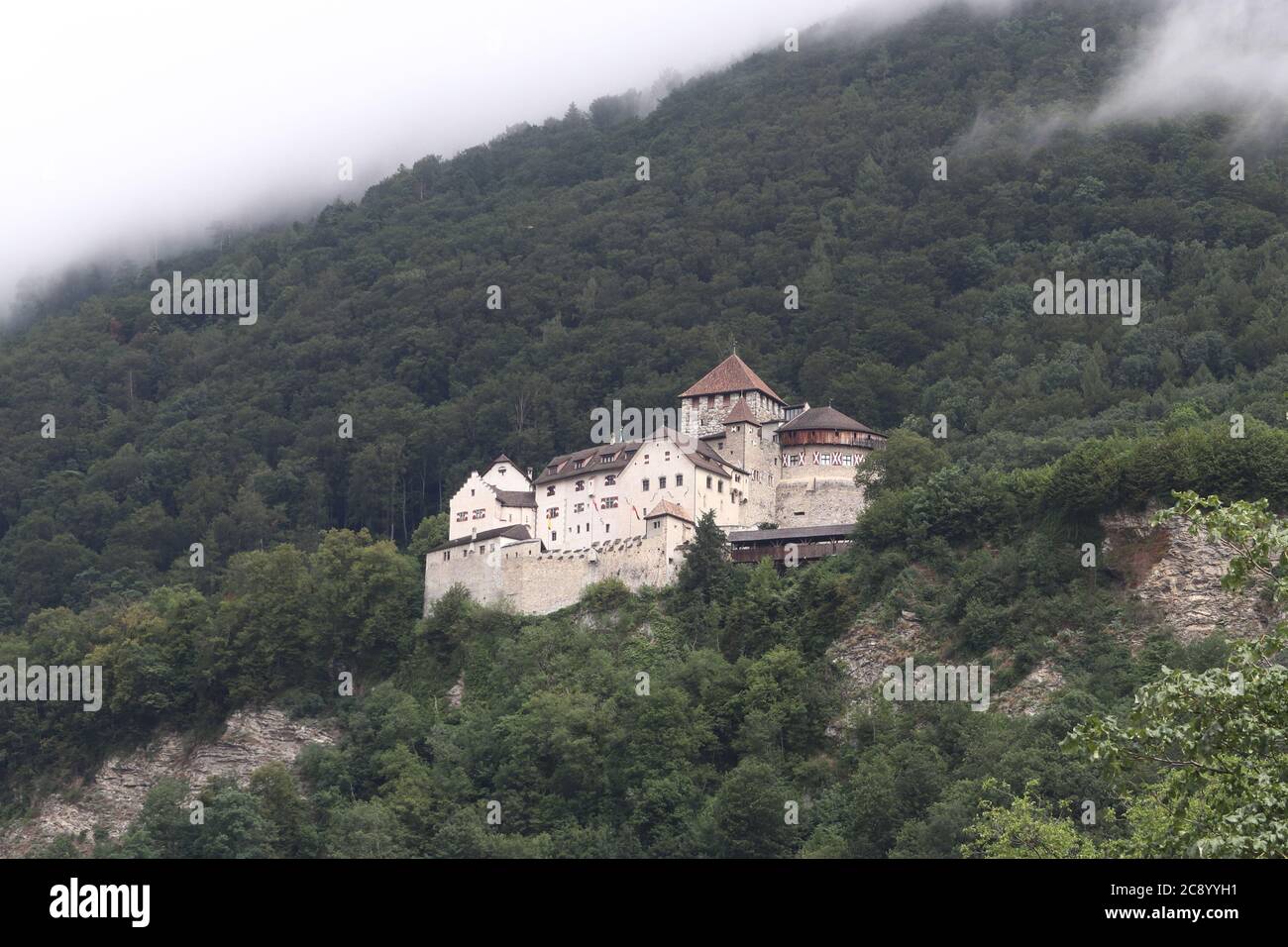 Vaduz / Liechtenstein - August 10 2019: Castle of Vaduz high in the mountain on top of town Vaduz, trees covered in clouds Stock Photo