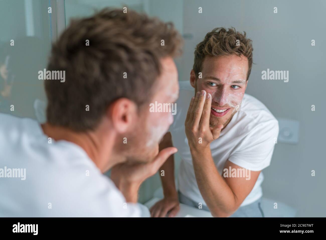 Man washing face with soap scrubbing exfoliation mask facial treatment looking in the mirror. Men taking care of skin, morning face wash routine for Stock Photo