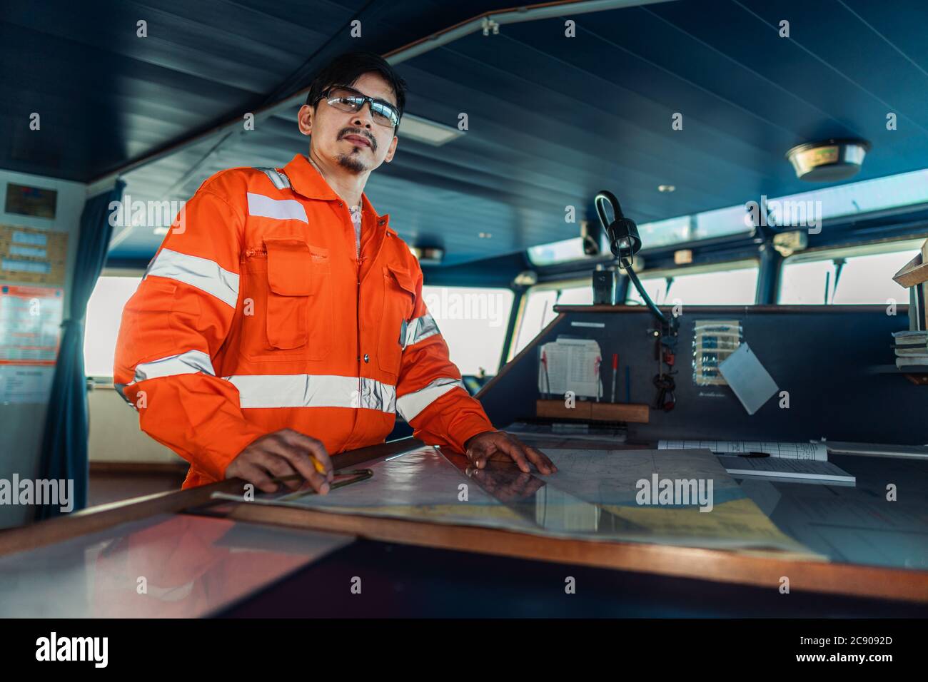 Filipino deck Officer on bridge of vessel or ship. He is plotting position on chart Stock Photo